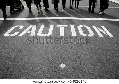 a caution sign on the street with the silhouette of peoples feet in the background