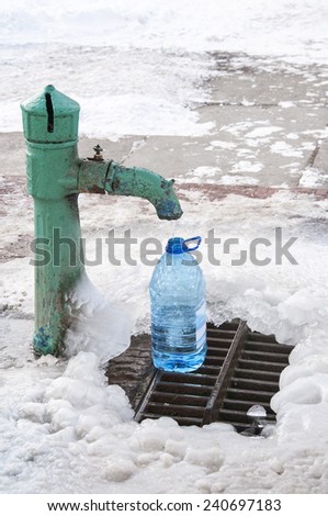 Street water tap pouring water into plastic container, winter time