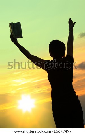 female praying with bible against summer sunset