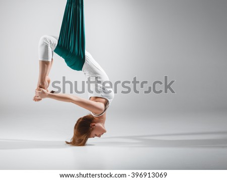 An adult woman practices different inversion - anti-gravity yoga positions in a bright well lit studio.