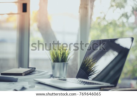 Business work table in office with laptop computer , notebook , and a cup of artificial grass for creative business work or marketing plan to success planning of company