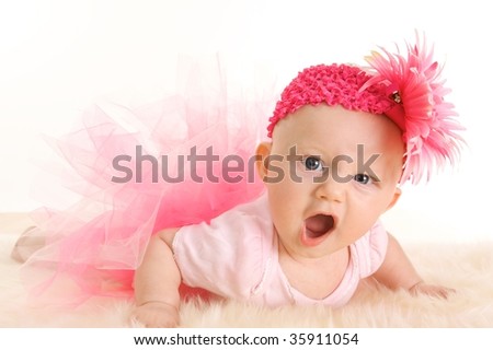 Cute young infant girl in a pink tutu and head band with an angry game face
