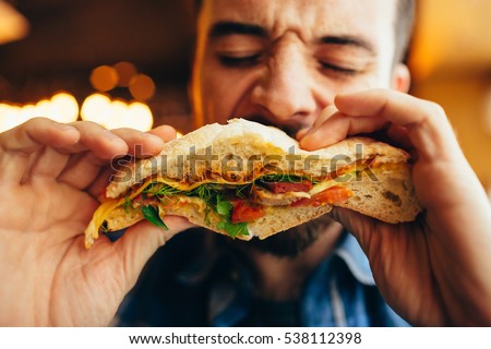Man in a restaurant eating a hamburger, he is hungry and having a good bite. Burger dinner