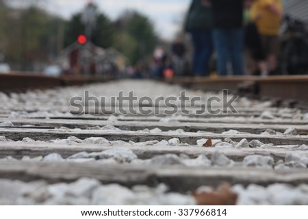 A view down the length of train tracks from ground level with people waiting on the side.