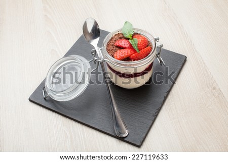 Delicious traditional italian cream dessert pannacotta with grated chocolate, strawberry, and basil served in jar with cocktail spoon on black stone background