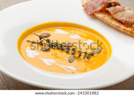 Pumpkin cream soup puree with ginger smack,  served in white plate , baked bread slice, bacon, seeds and  thyme