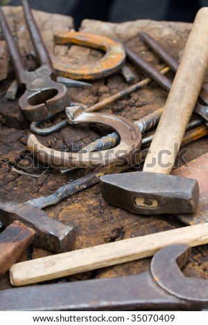 Rusty blacksmith tools and horseshoes on wooden log
