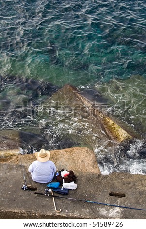 Fisherman in hat is sitting on the stone and fishing, top vertical view