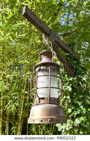 Street aged vintage copper kerosene oil lamp with glass bulb is hung up batten outside on the green leaves background