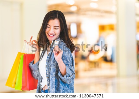 Happy beautiful Asian woman smile at credit card, hold shopping bags, copy space on shopping mall background. Shopaholic people, retail special offer price, holiday vacation activity lifestyle concept