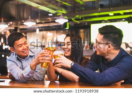 Group of happy Asian friends or office colleague coworkers celebrate toast beer pint together at pub restaurant or club. TGIF party, beer festival, team success event, or friendship lifestyle concept