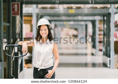 Beautiful young Asian engineer or technician woman smiling, warehouse or factory blur background, industry or logistic concept, with copy space