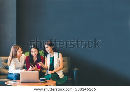 Three beautiful Asian girls using smartphone and laptop, chatting on sofa at cafe, with copy space, modern lifestyle with gadget technology or working woman on casual business concept