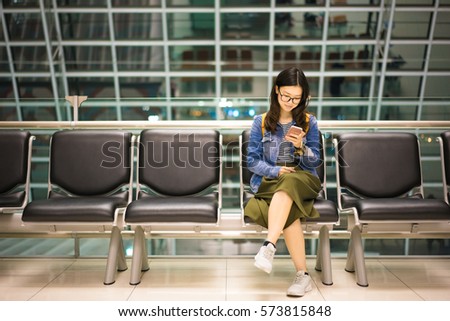 Beautiful Asian college student holding smartphone, waiting for flight at airport, travel or study abroad concept, with copy space.