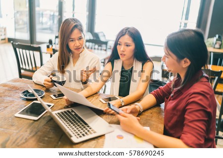 Group of young Asian women, college students in serious business meeting or project brainstorm discussion at coffee shop. With laptop computer, digital tablet, smartphone. Startup or teamwork concept.