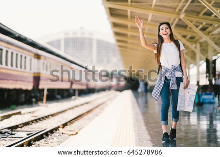 Asian backpack traveler woman holding generic local map and waving hand at train station platform, summer holiday travelling or young tourist concept