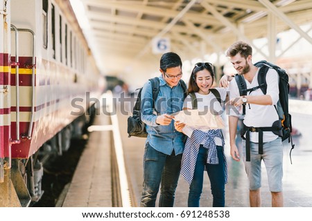 Multiethnic group of friends, backpack travelers, or college students using local map navigation together at train station platform. Asia travel destination, tourism activity, or railroad trip concept