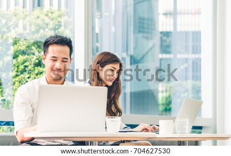 Young Asian couple or college student using laptop computer notebook work together at coffee shop or university campus. Information technology, cafe lifestyle, office meeting, or e-learning concept