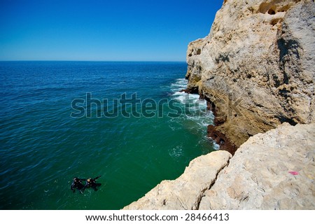 Cliff at Algarve coast in Portugal with two divers in water.