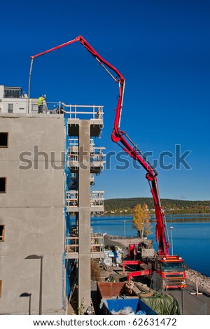 Huge concrete pump with tall arm pumping concrete on top of the building with workers