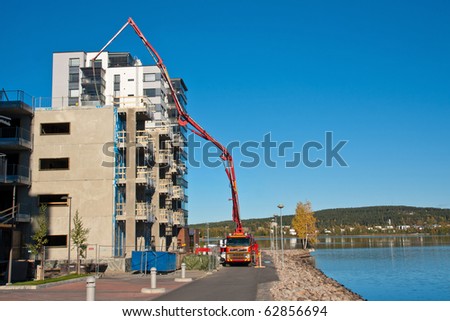 Huge concrete pump with tall arm pumping concrete on top of the building with workes