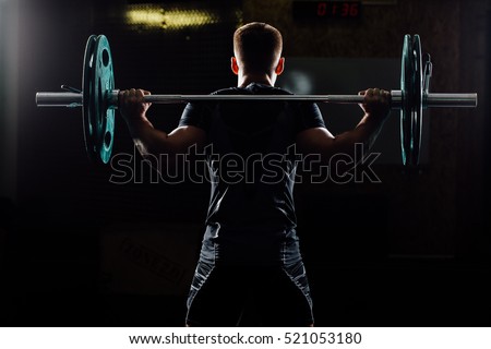 Handsome weightlifter training. Confident muscular man training squats with barbells over head. Closeup portrait of professional bodybuilder workout with barbell at gym. Back view, Silhouette.