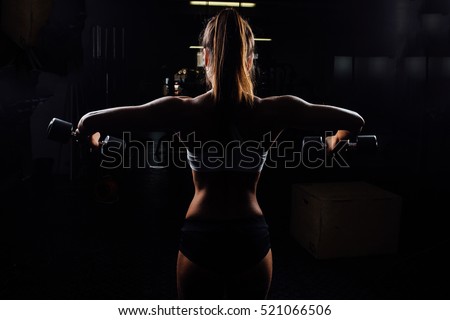 Beautiful fitness woman with lifting dumbbells . Sporty woman lifting light weights. Fit girl exercising building muscles. Fitness and bodybuilding. Back view. Silhouette