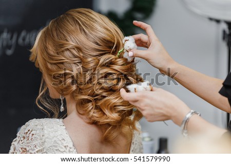 Hair stylist or florist makes the bride a wedding hairstyle with fresh cotton flowers