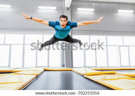 A young fit happy man jumping and flying on trampoline in fitness gym
