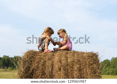 Two little sisters against the blue sky in summer day play with each other