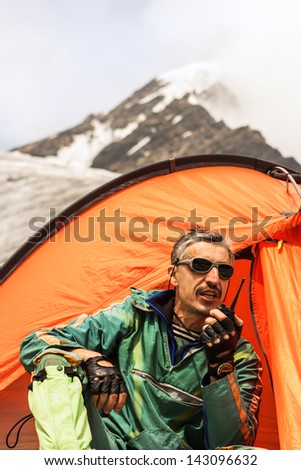 The climber near tent speaks on handheld transceiver with other climbers