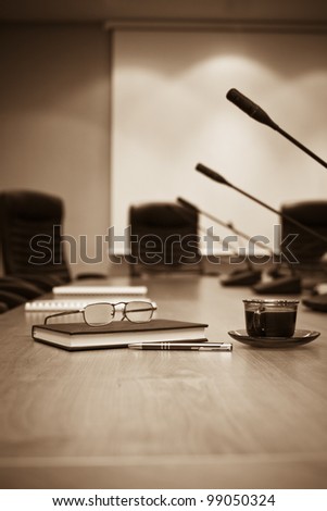 A close-up of a conference room showing a chairs, a table, a coffee cup,  and a note pad. Sharp focus on the cup.