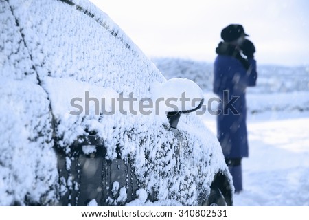 A woman calls for the breakdown services near her snow covered motorcar.