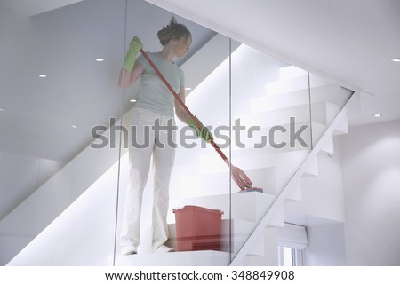 Female cleaner works in a modern home / office environment mopping the stairs