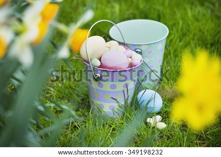 Children\'s bucket filled with painted eggs from an Easter egg hunt, with spring daffodils in the foreground.