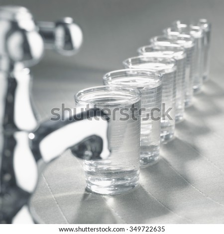 Close up of a kitchen tap and several glasses filled with fresh clean water to illustrate the daily required intake advised by the medical profession.