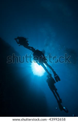 Silhouette of three scuba divers in blue water.