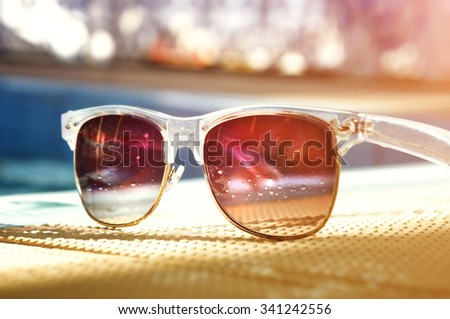 Dark tinted sunglasses with drops of water reflecting pool. Bright sunny day.