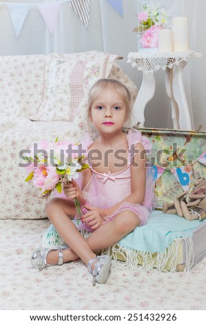 Little girl sitting on small bag with flowers in pink dress