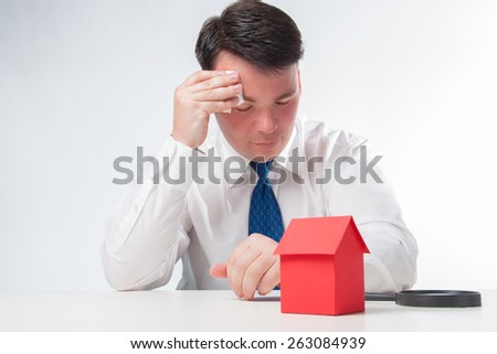 Sad Man with a magnifying glass and paper house. Real estate concept on a white background
