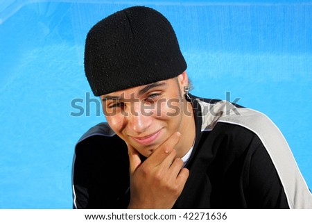 a happy teenager with a cap and a wart at his index finger, photographed in the summer sun sitting at a swimming pool giving us a happy and satisfied smile
