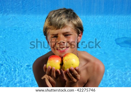 a 10-years old smiling American - German boy sitting at a swimming pool and presenting delicious apples in the summer sun