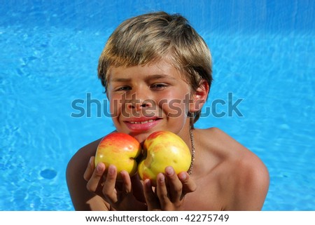 a 10-years old smiling American - German boy sitting at a swimming pool and presenting delicious apples in the summer sun
