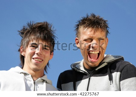 two teenagers making fun, one smiling and the other one laughing with his mouth wide open , photographed in the summer sun with blue sky in the background
