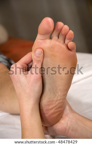 closeup of a foot of a natural mature woman having a foot reflex zone massage at the ball of the foot