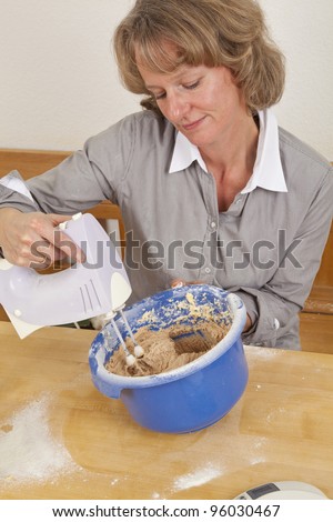 smiling woman mixing dough with electric hand mixer