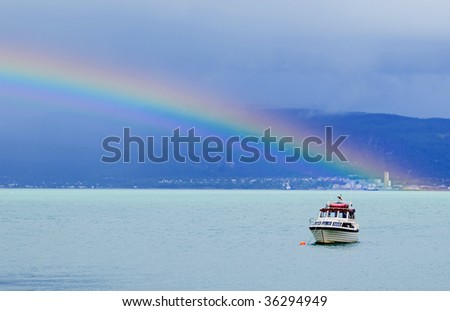 Bright rainbow over sea with boat in front