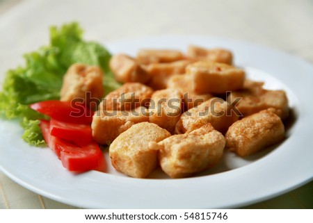 White platter with chicken bites, tomatoes and green salad on white tablecloth