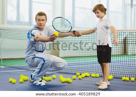 Instructor or coach teaching child how to play tennis on a court indoor