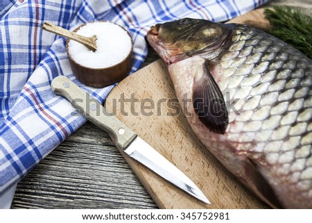 A large fresh carp live fish lying on a wooden board with a knife and slices of lemon and with salt dill